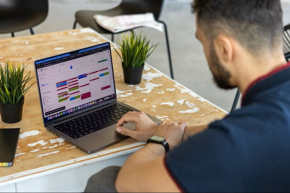 Man using employee scheduling software on a laptop calendar in a modern co-working space.