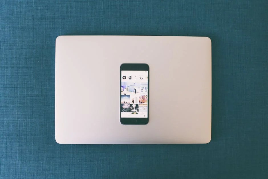 A flat-lay image of a dark smartphone displaying a social media feed, placed on a closed silver laptop. Both are set against a textured blue background, creating a clean and minimalistic aesthetic, illustrating how to use social media for small business effectively.