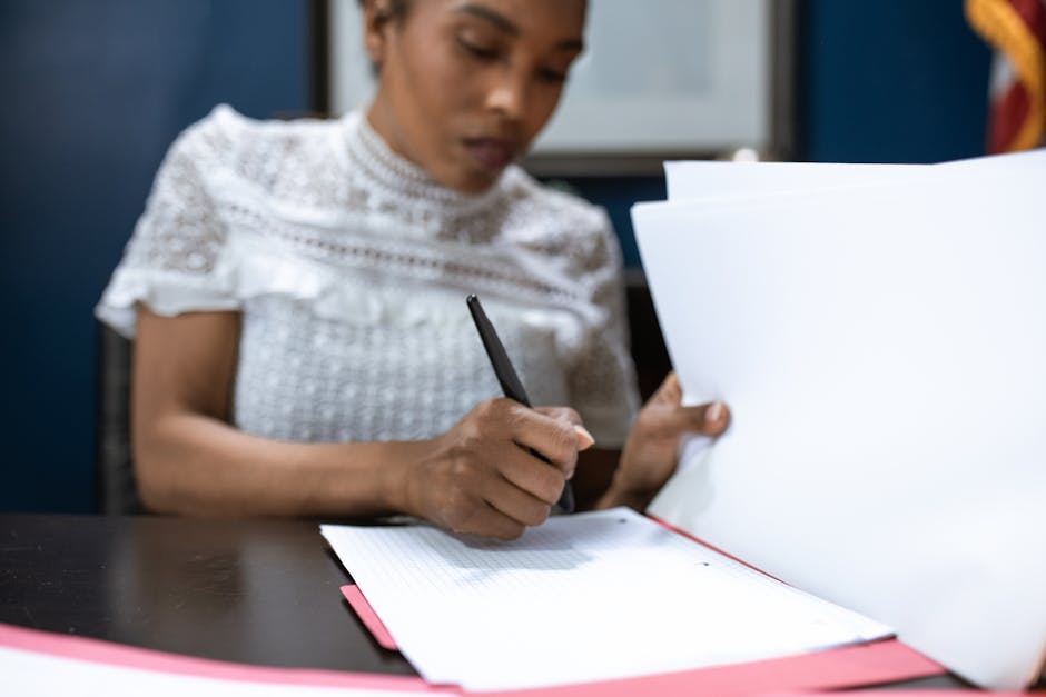 Woman signing or reviewing Small Business Administration documents at a desk with a flag in the background.