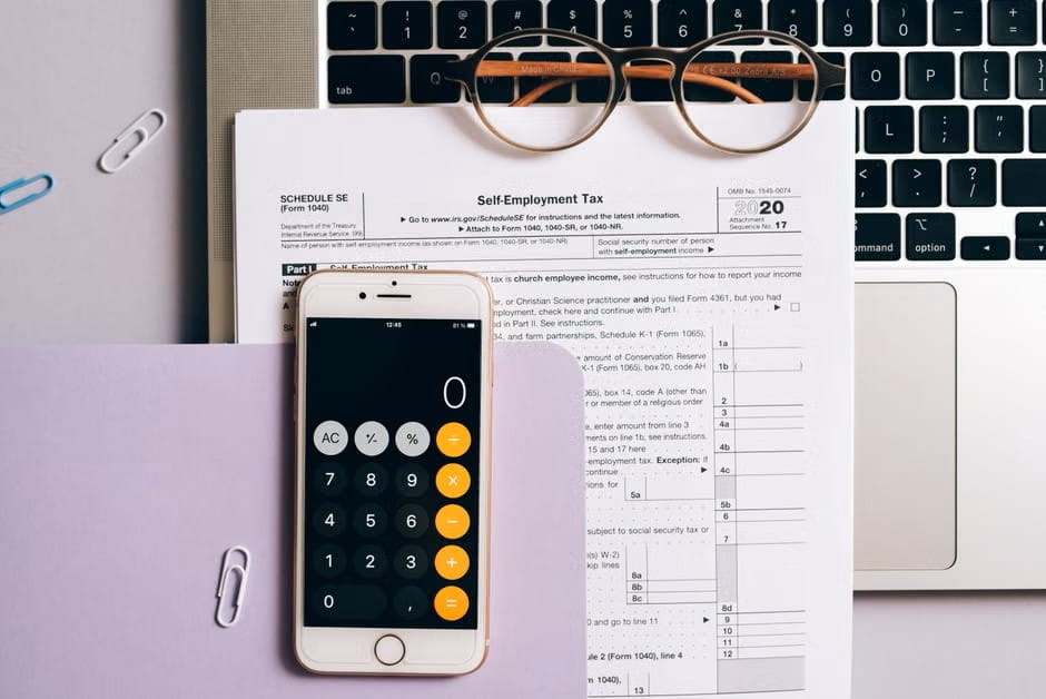 overhead workspace with tax form, calculator phone, and laptop for researching the best small business accounting app.