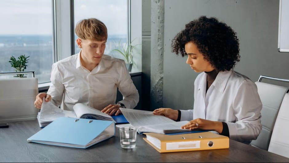 two professionals reviewing binders and documents while choosing the best small business accounting app.