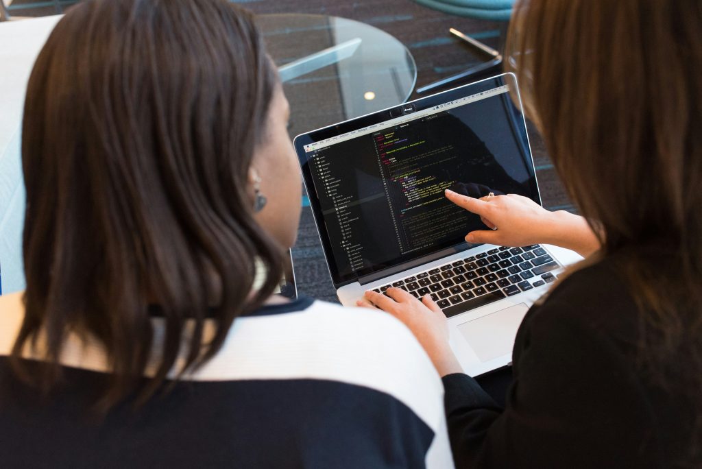 Two individuals collaborate on a MacBook Pro displaying Ruby code in the Atom editor, a perfect example of effective information management for small business. One points at the screen while the other interacts with the keyboard, emphasizing teamwork in a coding environment.