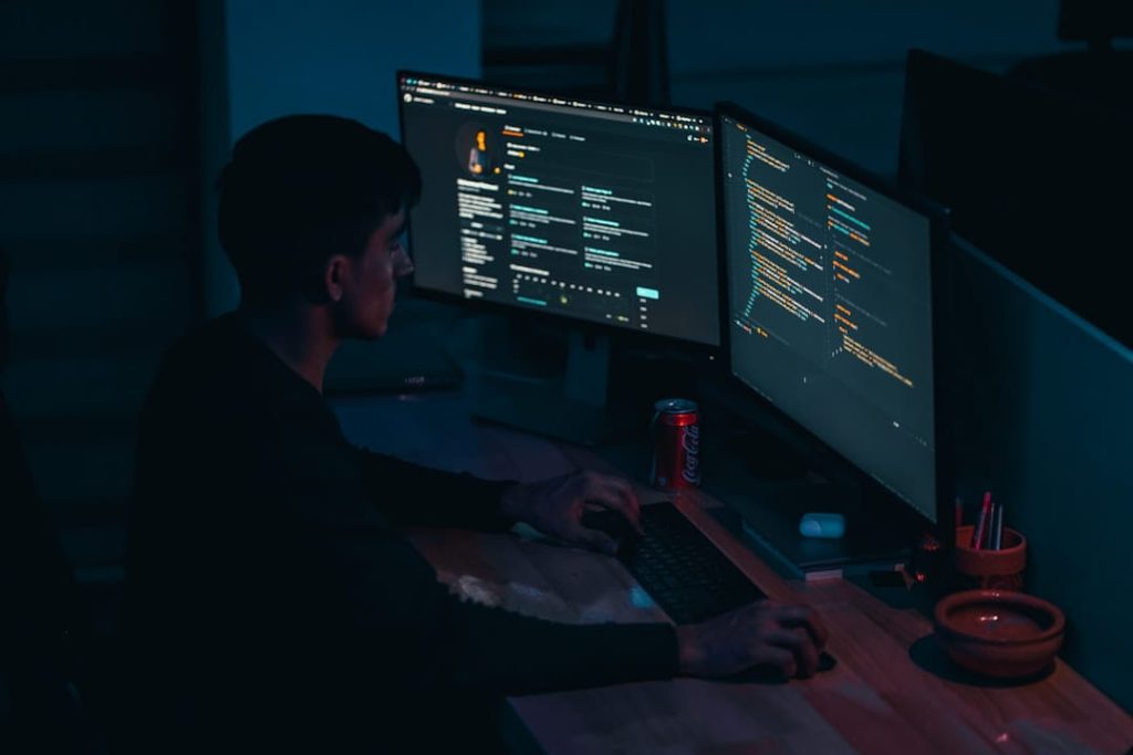 Developer working at dual monitors with code and system data related to conversational AI platforms.