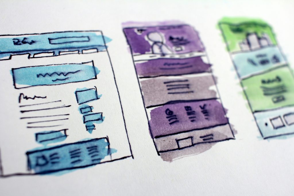Three sketched webpage or app design concepts arranged horizontally. Each sketch features distinct layouts with sections resembling headers, text blocks, and images. The left design is blue-themed with a large header and multiple rectangular blocks below. The middle design is purple-themed, showcasing a large icon or figure at the top and vertically stacked sections. The right design is green-themed, with a simplified structure and a large rectangular area at the bottom. The image serves as a brainstorming tool for visual design for a content marketing agency.