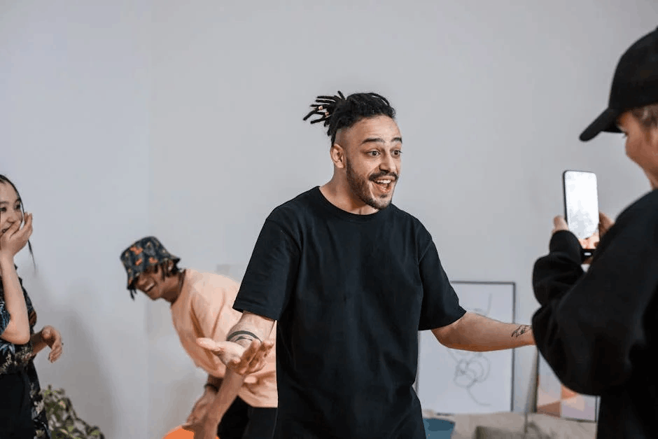 Casual group interaction with a man being filmed while others laugh in a bright room, discussing how to create a social media content calendar.