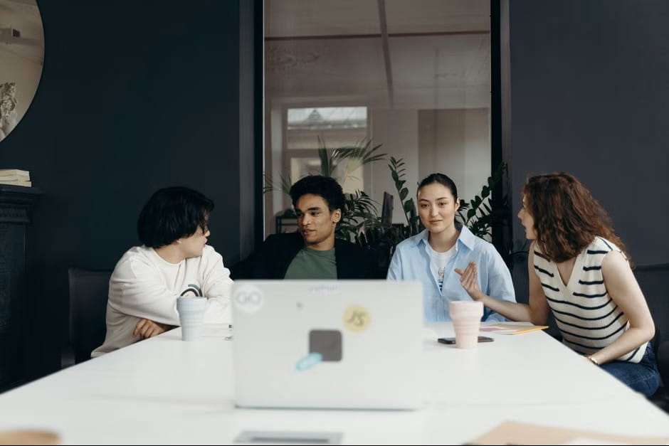Four diverse professionals hold a collaborative meeting around a white conference table in a modern office, mapping out how to create a startup together.