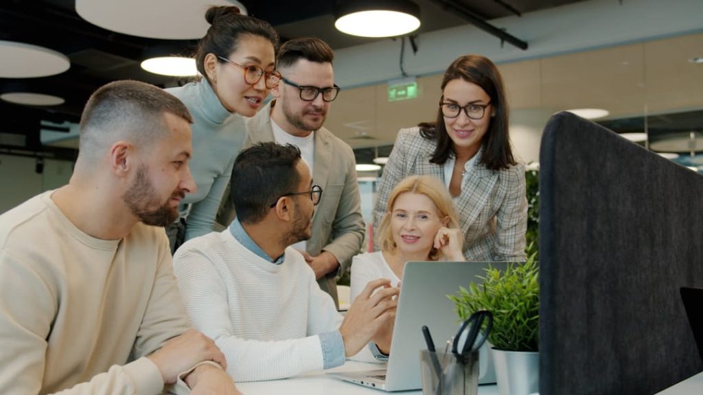 Team of six professionals collaborating around a laptop, discussing how to grow a business.