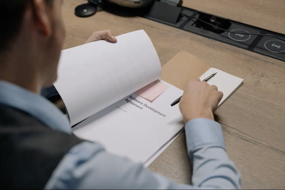 A man carefully reviewing a bound document at a modern office desk as he refines a job description template.