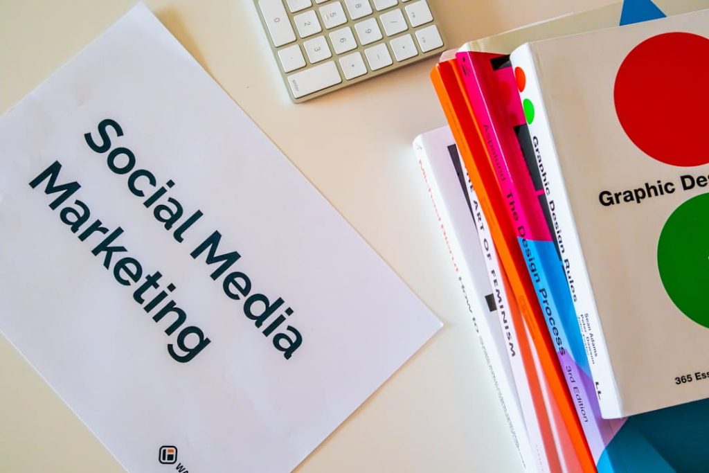 A desk with a paper on Metrics for Social Media Marketing, keyboard, and colorful books, suggesting a creative workspace.