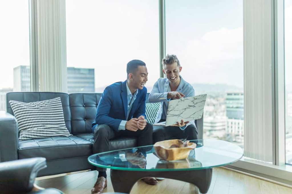 Two men smiling at a laptop in a high-rise office while reviewing a non disclosure agreement template.