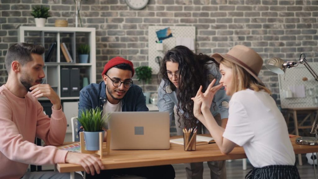 Four professionals gathered around a laptop in a creative office, reviewing their Shopify SEO checklist together.