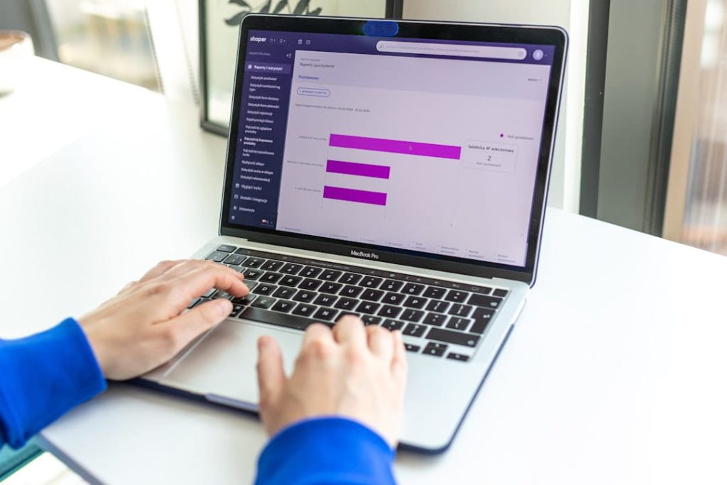 Hands typing on a MacBook that displays an e-commerce sales analytics dashboard, tracking progress on a Shopify SEO checklist.