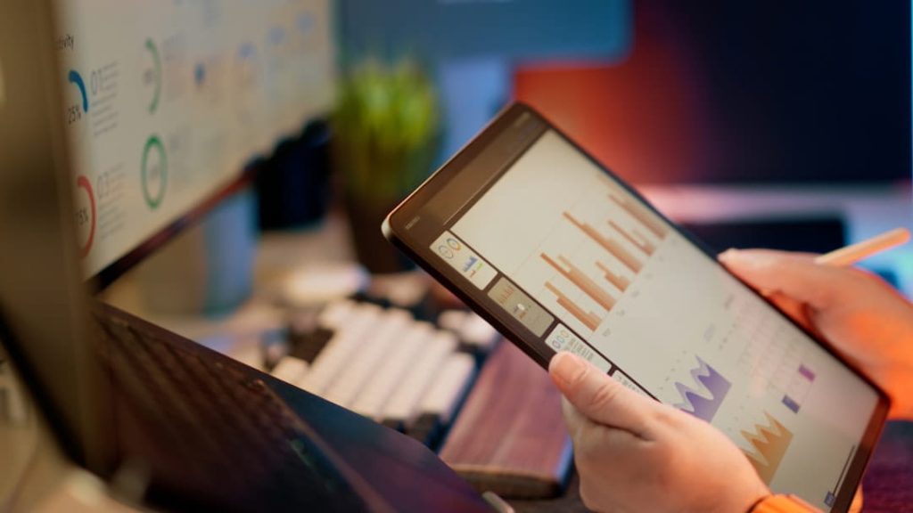 Hands using a tablet and stylus to review data dashboards across multiple screens while working through a Shopify SEO checklist.