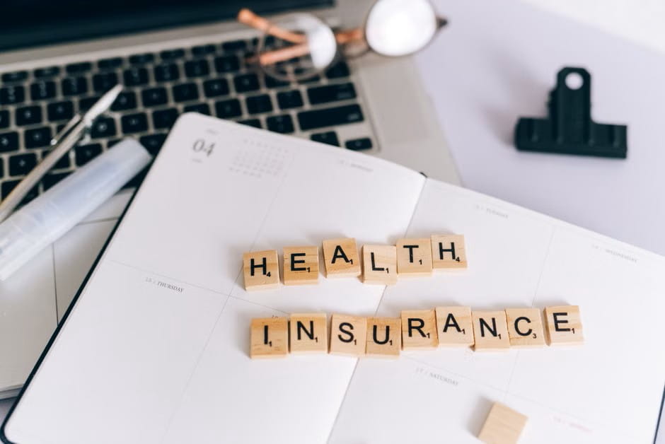 Small business health plans concept with health insurance tiles on an open planner beside a laptop and office supplies.