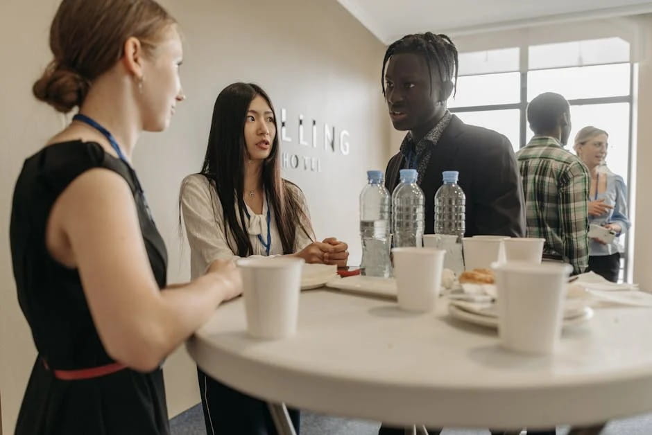 A group of professionals networking around a table at a Small Business Month hotel event, with lanyards and refreshments visible.